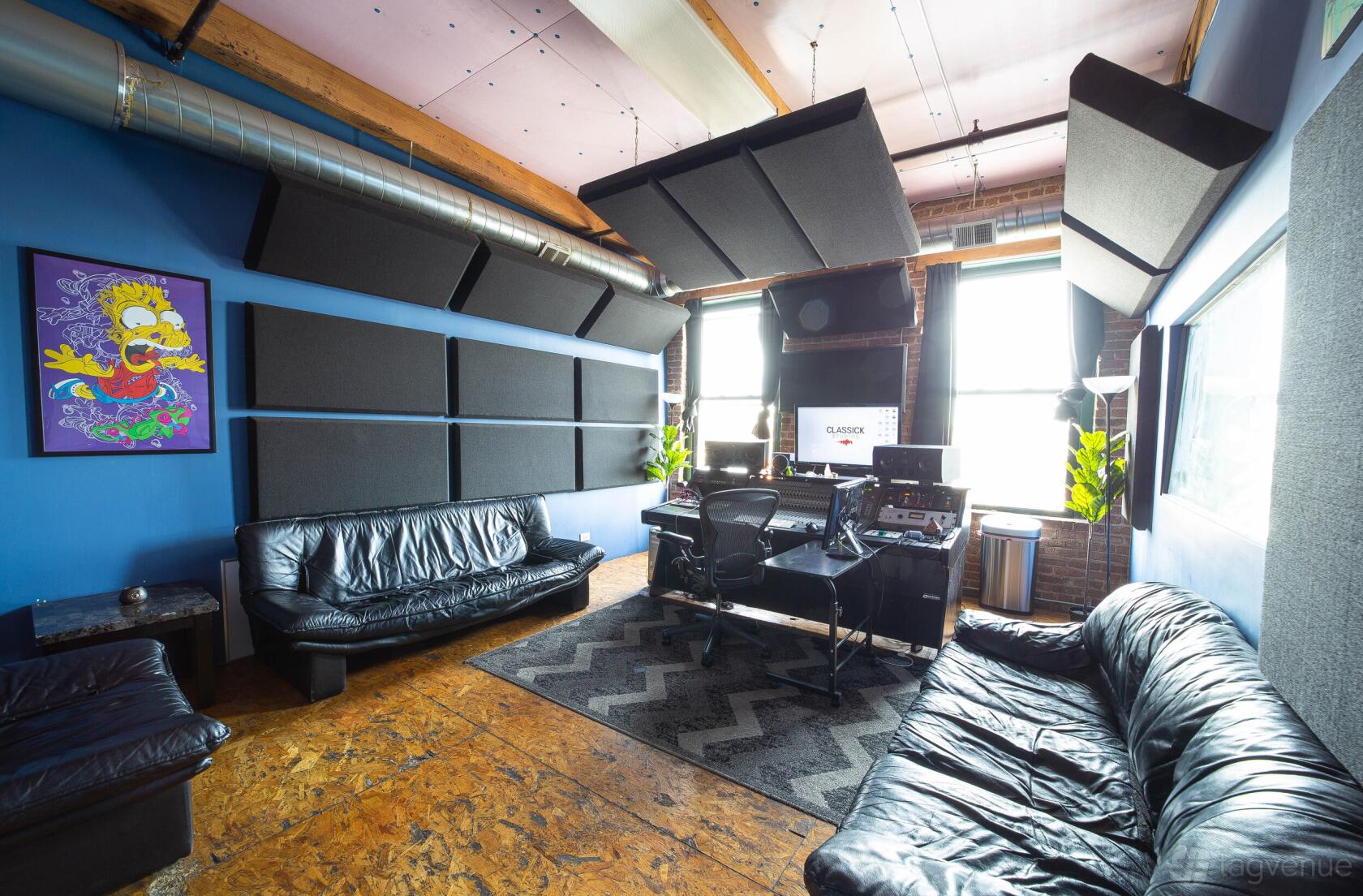 A recording studio with black leather sofas, acoustic panels, large windows, and mixing equipment at Classick Studios.