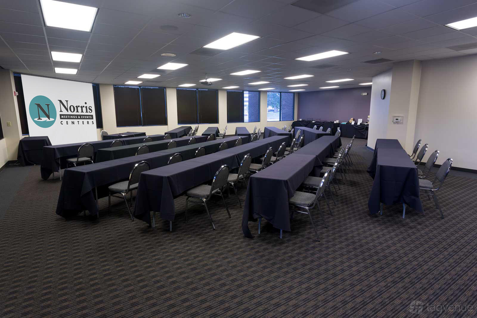 A conference room with long tables covered in dark linens, rows of chairs, and a presentation screen at Norris Conference Centers – Corporate.