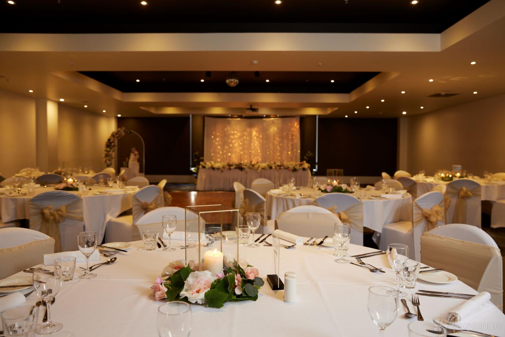 A banquet room with round tables covered in white linens, gold chair sashes, and floral centerpieces at Fountain Gate Hotel.
