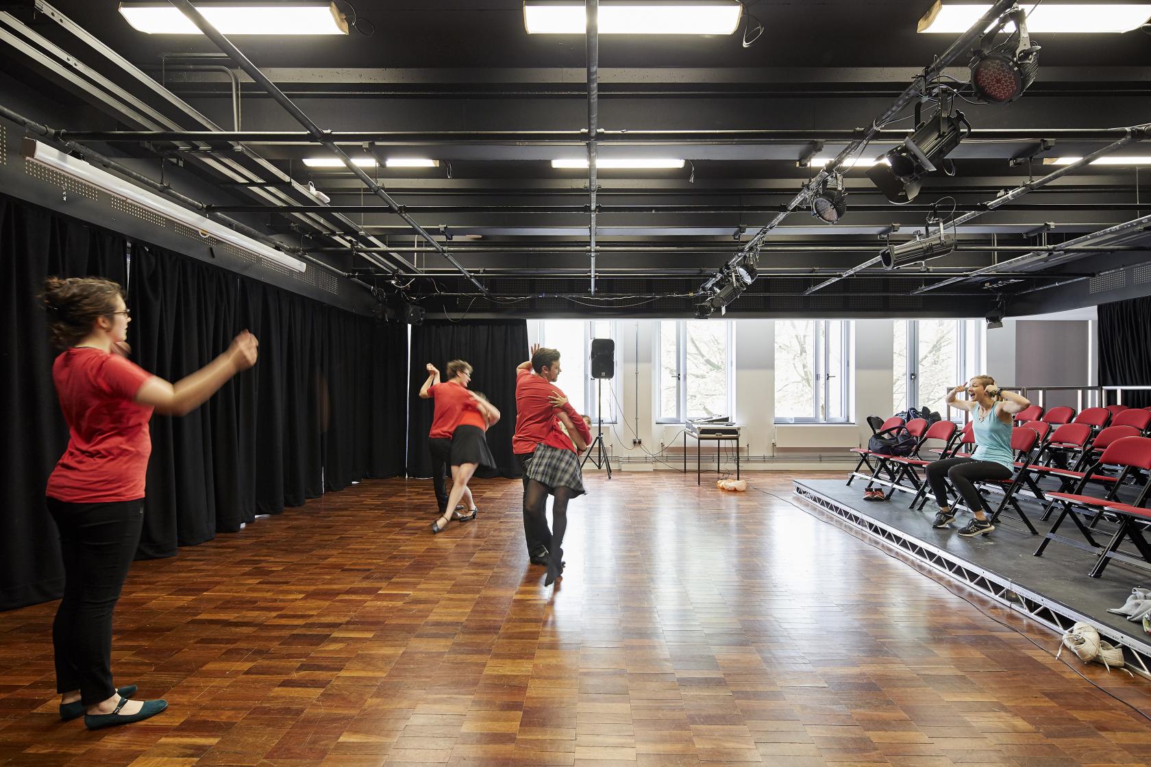A university theatre with parquet flooring, stage lighting, and red tiered seating at University of Bristol Students' Union.