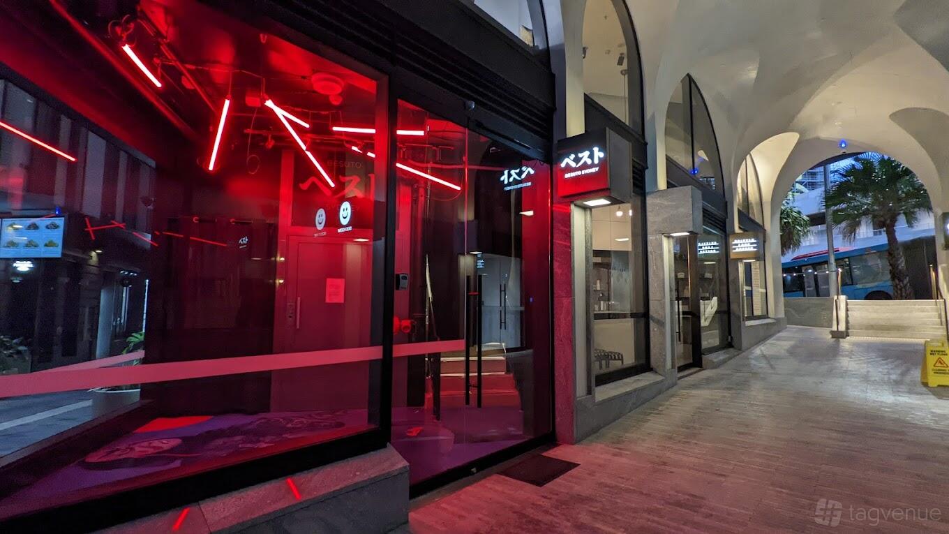A restaurant entrance with illuminated red neon lights and glass doors at Besuto - Omakase.