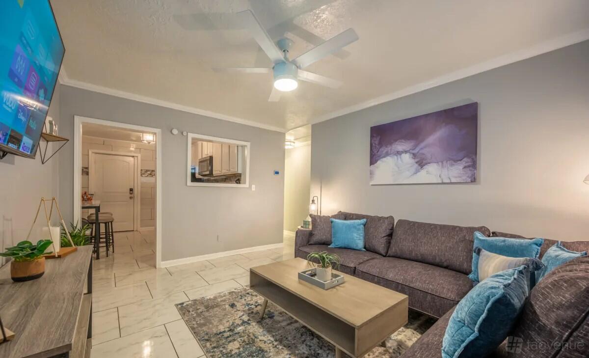 A house living room with a gray sectional sofa, blue accent pillows, wall art, and tiled floors at Suite Stays Atlanta - Welch St. Atlanta.