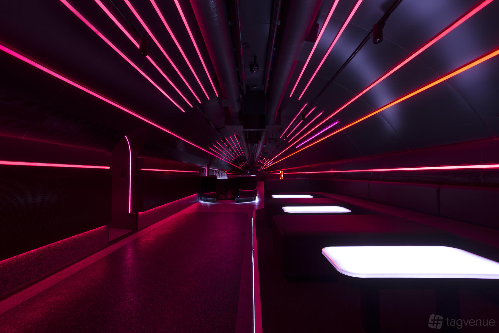 A nightclub event space with neon pink and red strip lighting, dark seating booths, and glowing white tables at Platform One Nightclub.