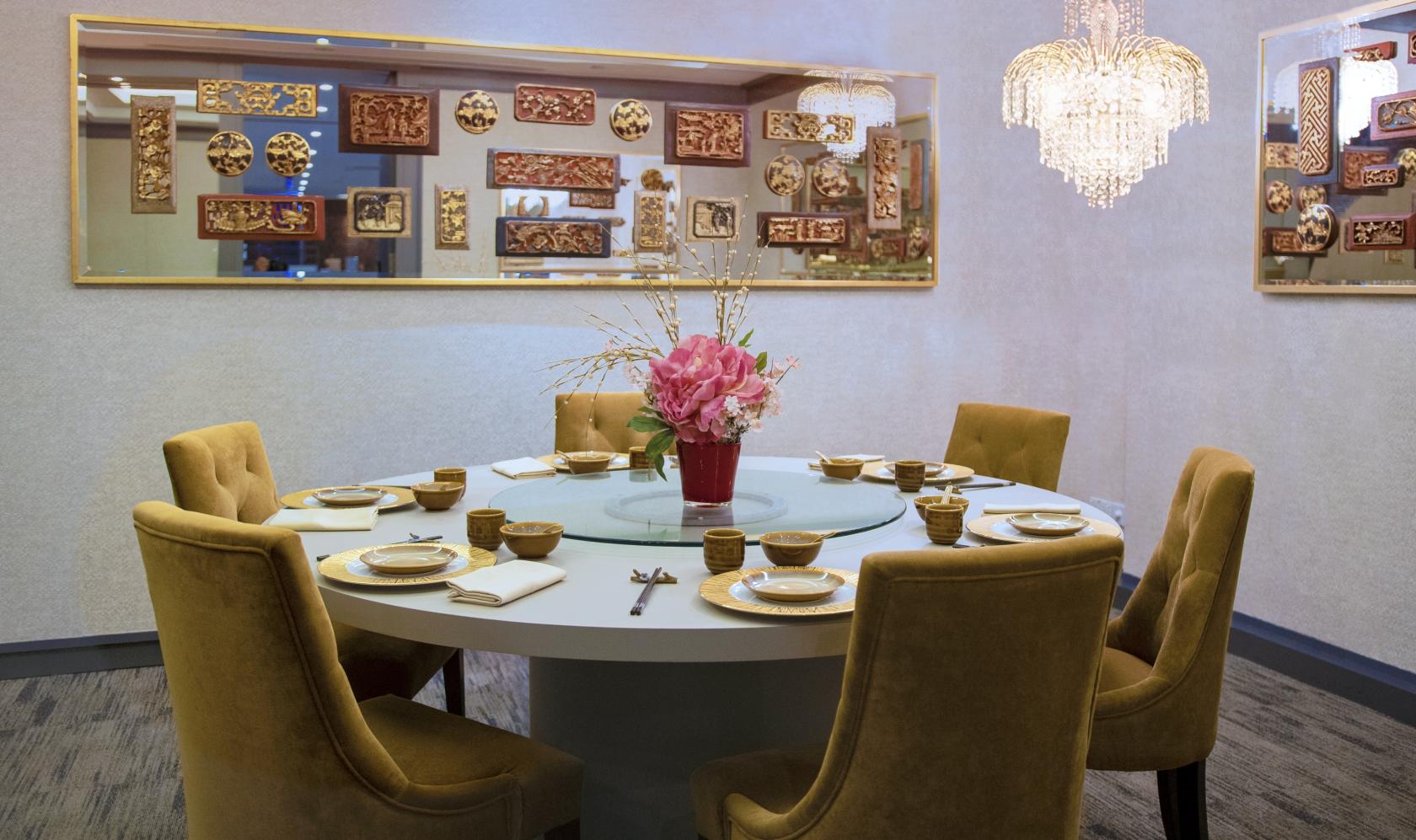 A private dining room with a round table set with gold tableware, velvet chairs, and a chandelier at Jia Wei Chinese Restaurant.