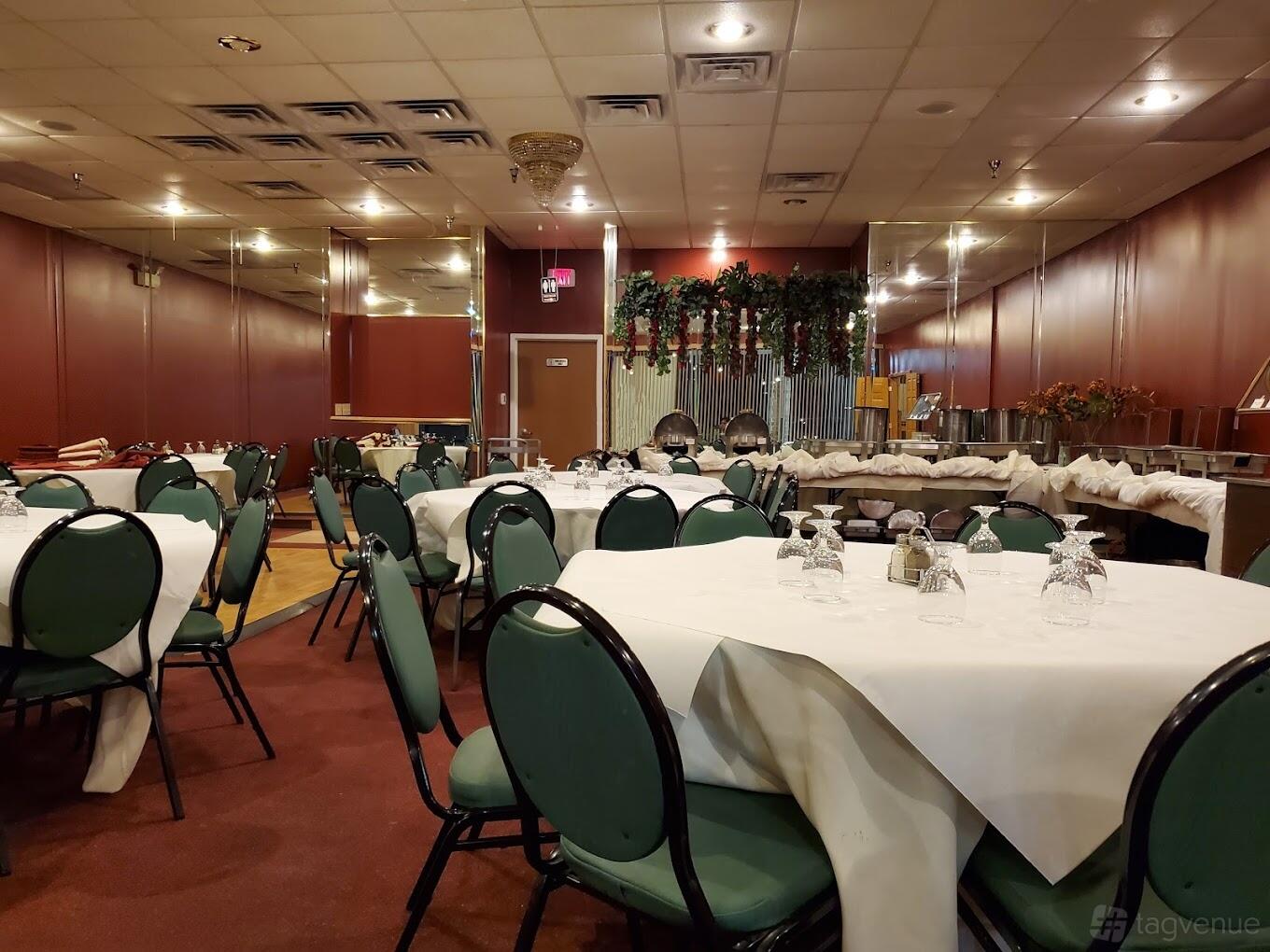 A banqueting hall with round tables covered in white linens, green cushioned chairs, and buffet stations at Taste of India Restaurant- Banquet & Catering.