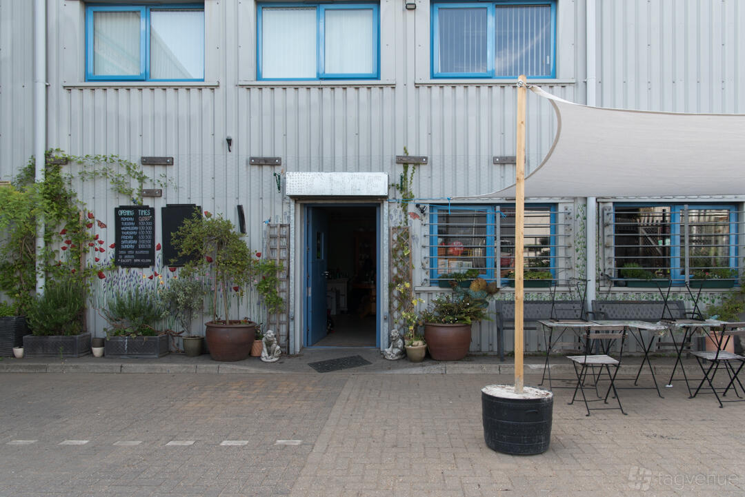 An outdoor cafe space with potted plants, metal tables and chairs, and a canopy at Old Station Yard Cafe.