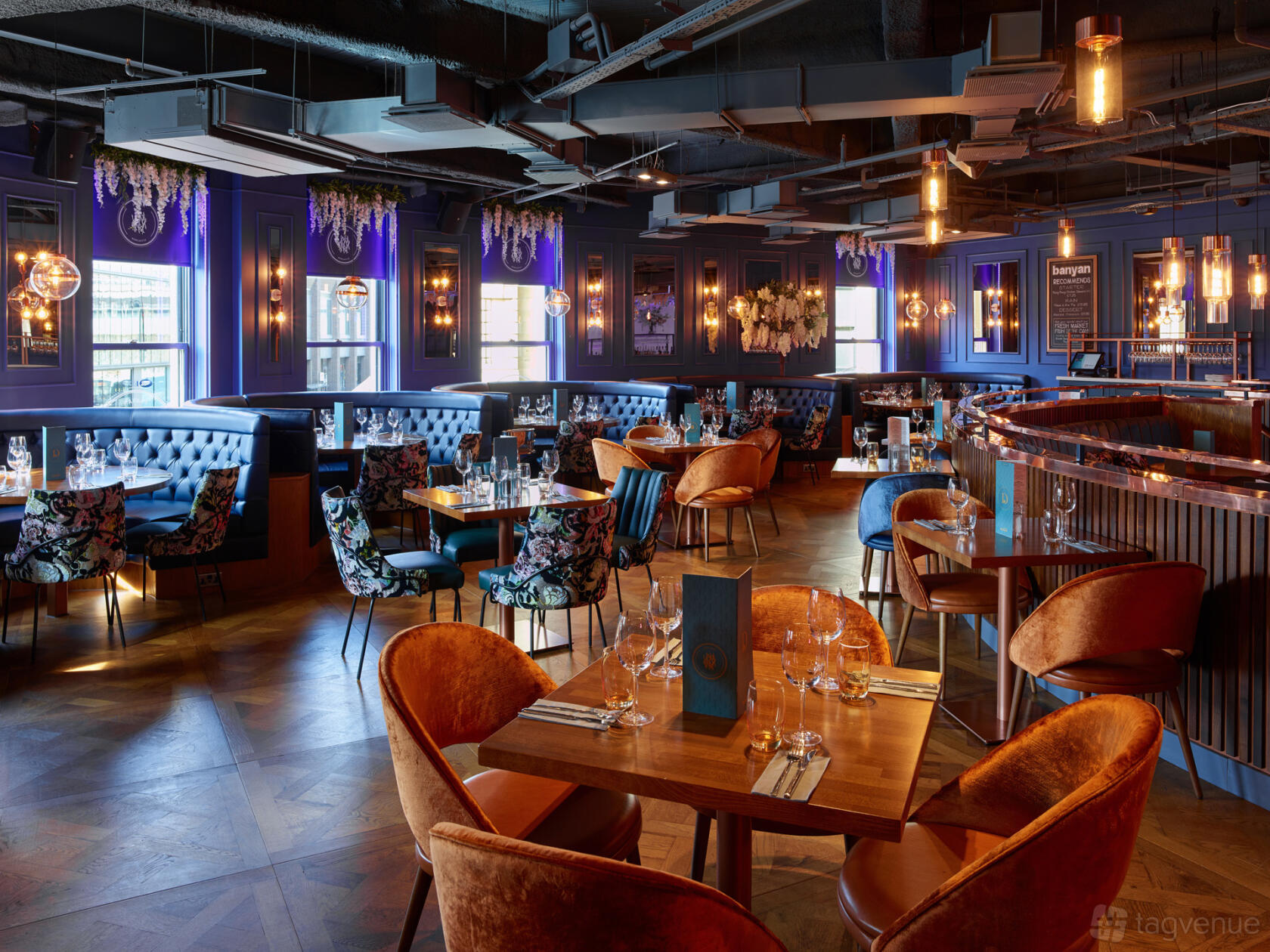 A restaurant bar with velvet chairs, banquette seating, floral decor, and pendant lighting at Banyan Newcastle.
