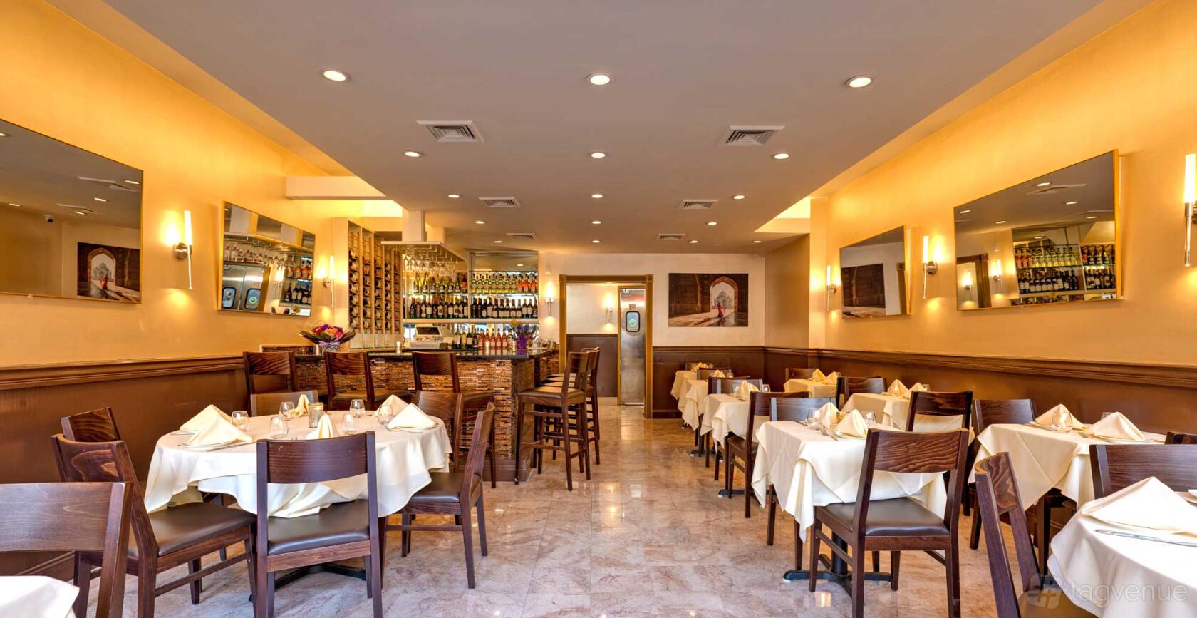 An event space in a restaurant with cream walls, mirrored accents, and tables draped in white linens at Jaz Indian Cuisine.