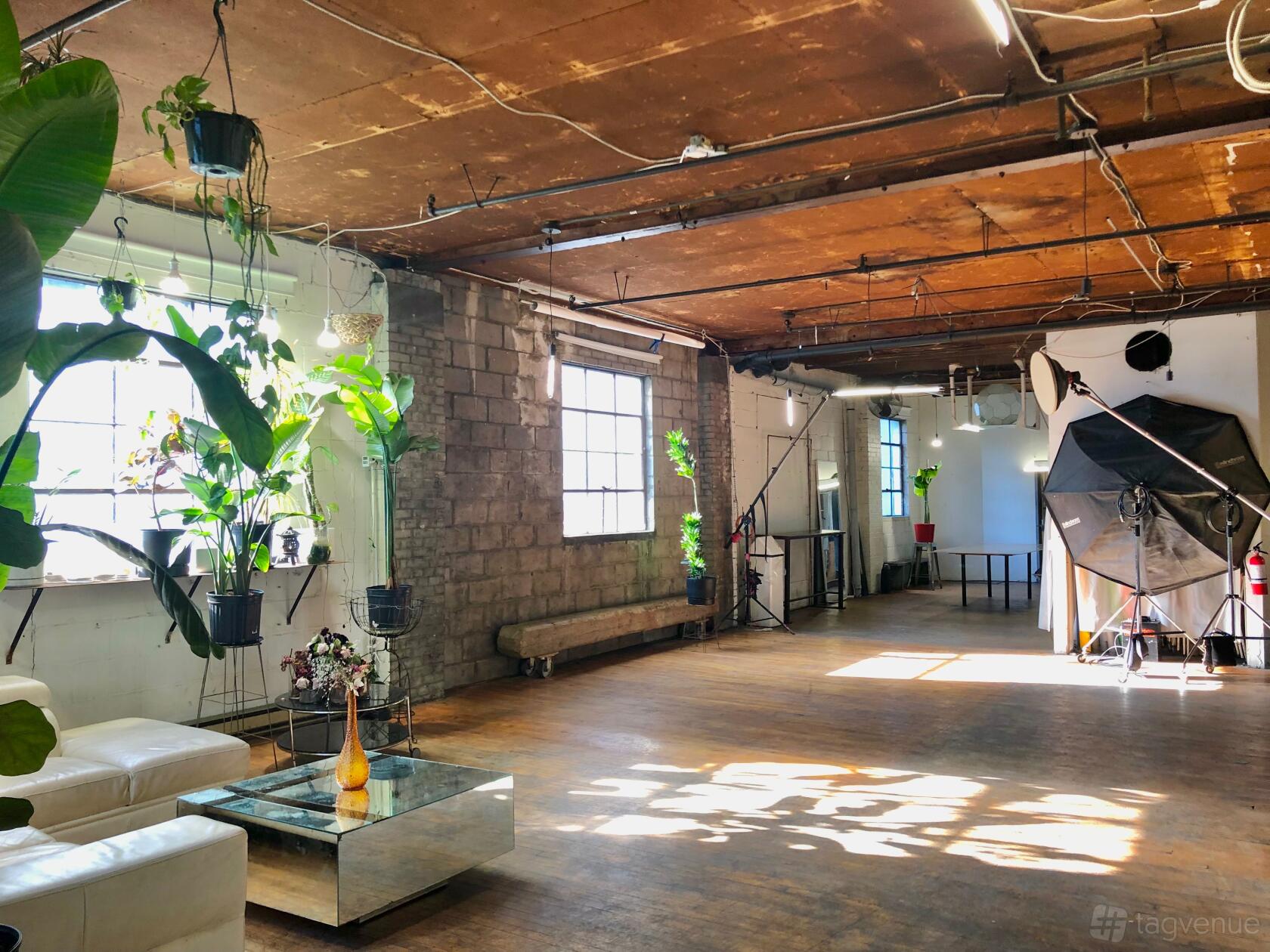 A photo studio with exposed brick walls, large windows, and lighting equipment at Diptych Studio.