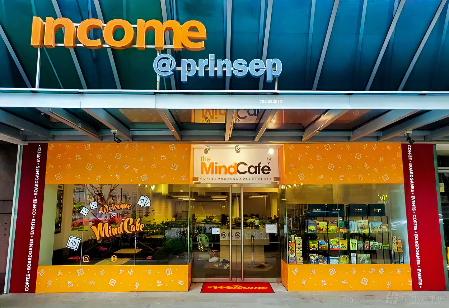 A café entrance with orange signage, glass doors, and a display of board games at The Mind Cafe Mega.