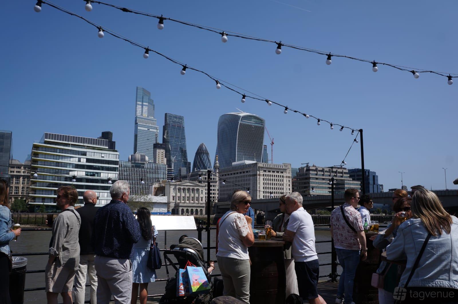 An outdoor pub area with string lights, wooden tables, and views of modern London skyscrapers at The Old Thameside Inn.