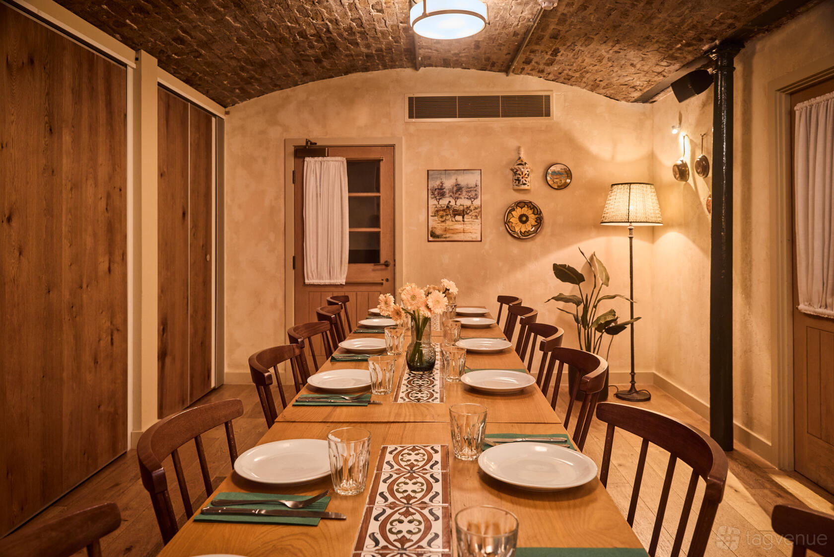 A dining room with a long wooden table, exposed brick ceiling, vintage wall decor, and soft lamp lighting at Casa do Frango - Mayfair.