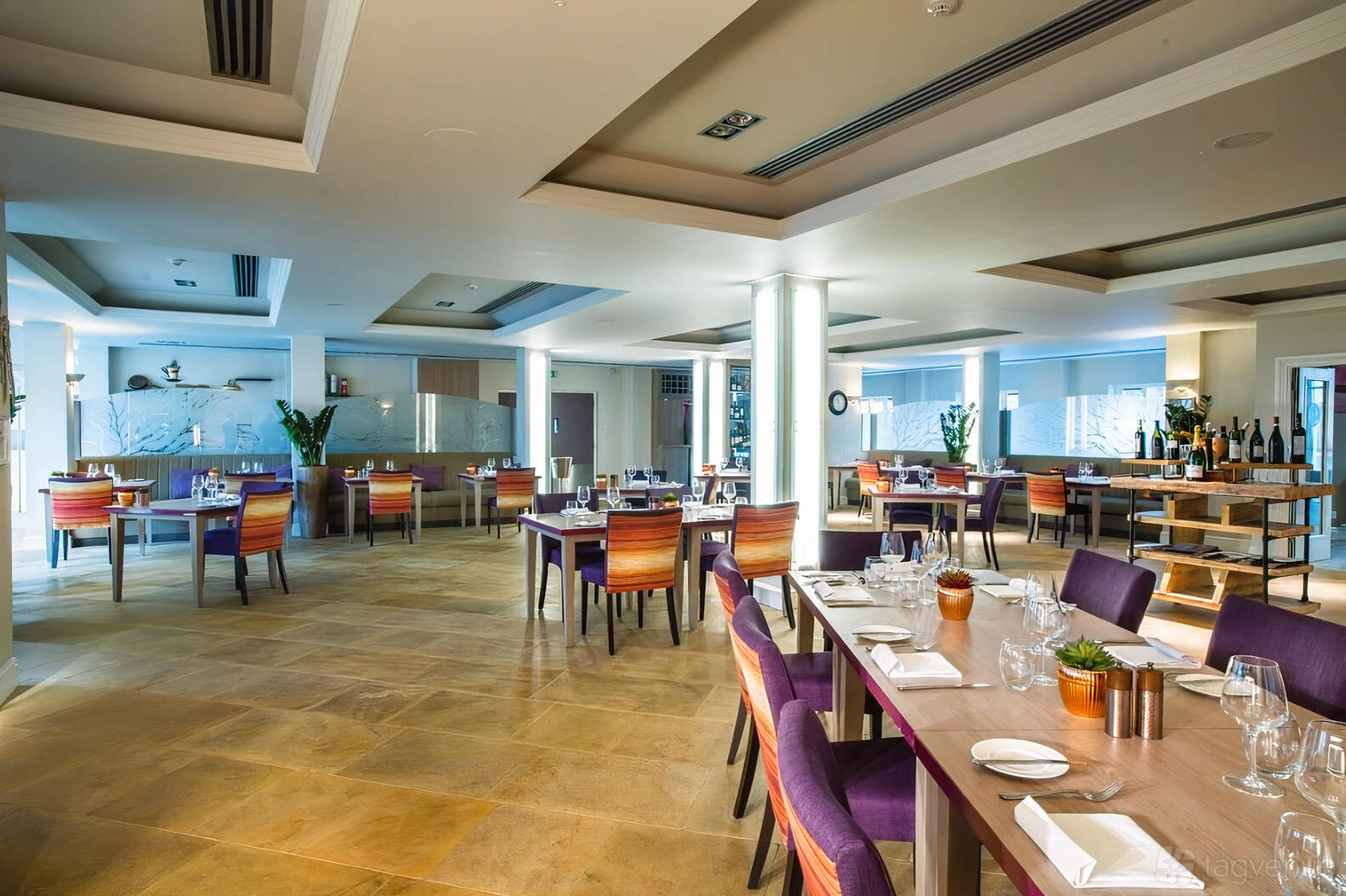 A restaurant dining room with wooden tables, purple chairs, set place settings, and large floor-to-ceiling windows at Sudbury House Hotel.