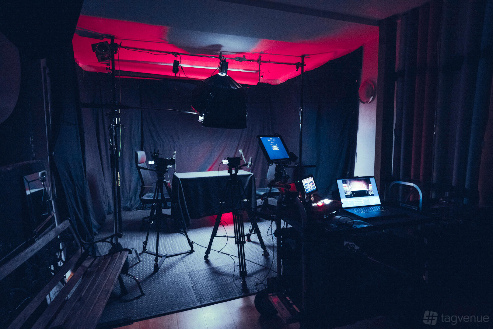A podcast studio with blackout curtains, professional cameras, microphones, and red accent lighting at Colores - London photo studio.