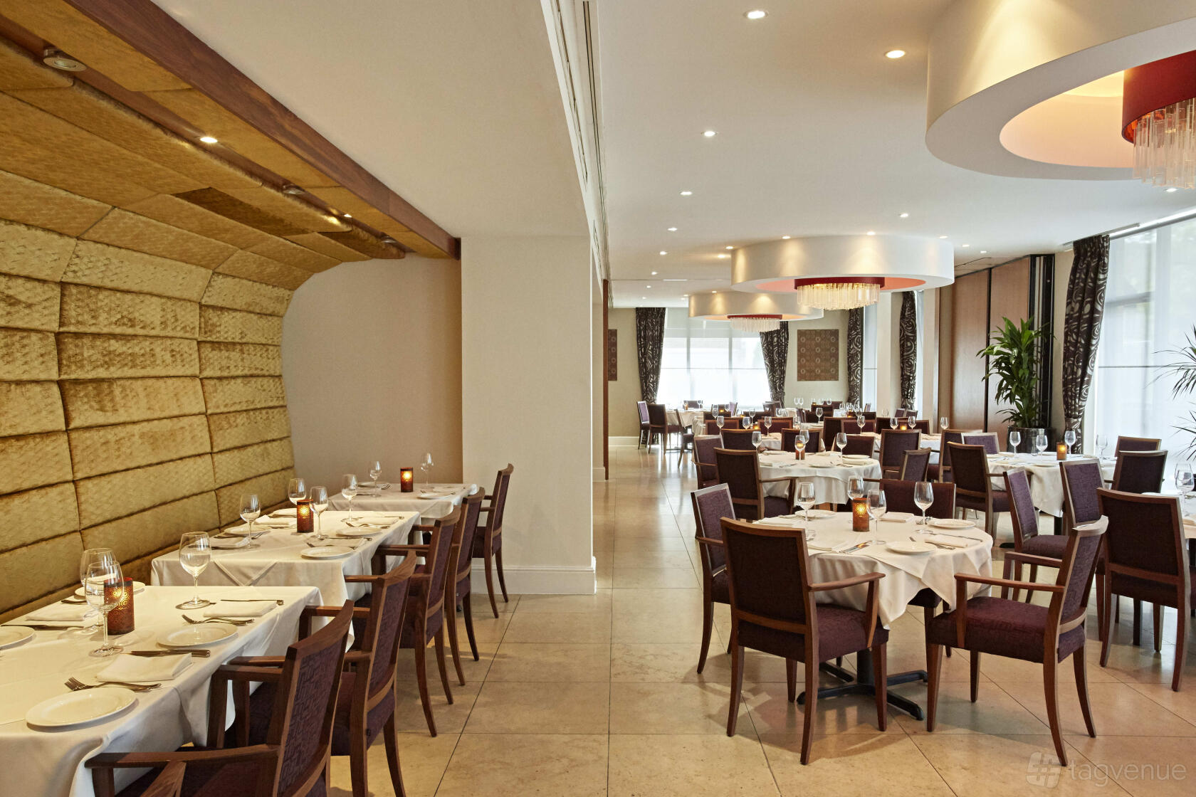 A restaurant dining room with white tablecloths, wooden chairs, chandeliers, and large windows at Bombay Palace.
