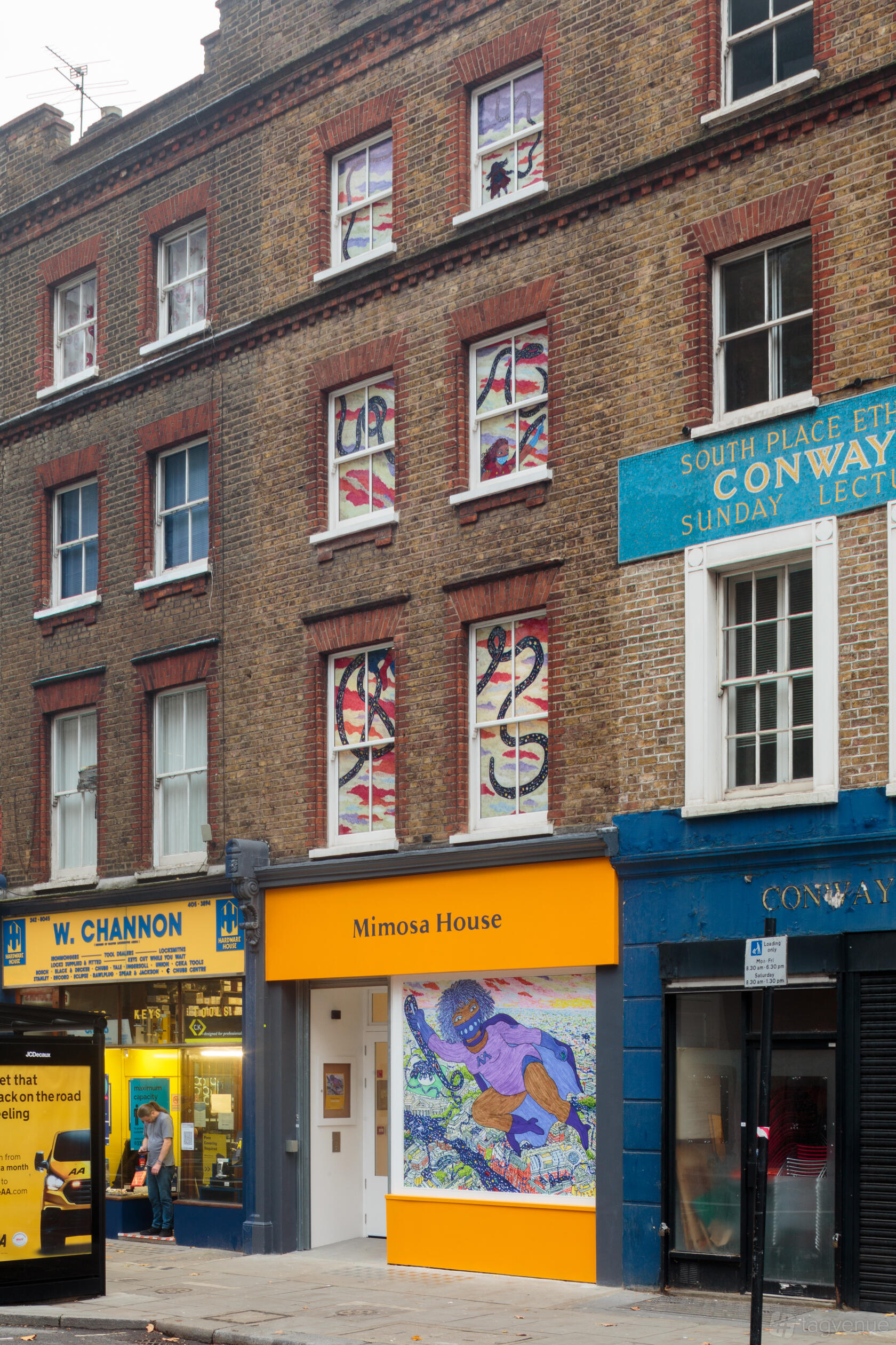 A gallery with a brick exterior facade and large front windows with abstract art at Mimosa House