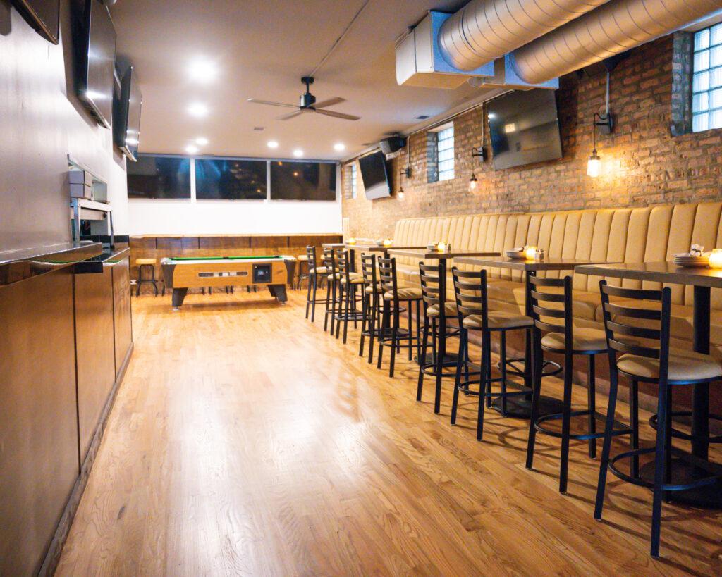 A restaurant with exposed brick walls, wooden floors, tan banquette seating, and high-top tables at Avenue Tap and Kitchen.