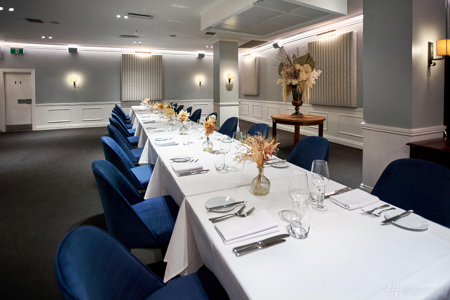 An event venue with a long table set with white linens, blue velvet chairs, and dried floral centerpieces at The Royal Exchange of Sydney.