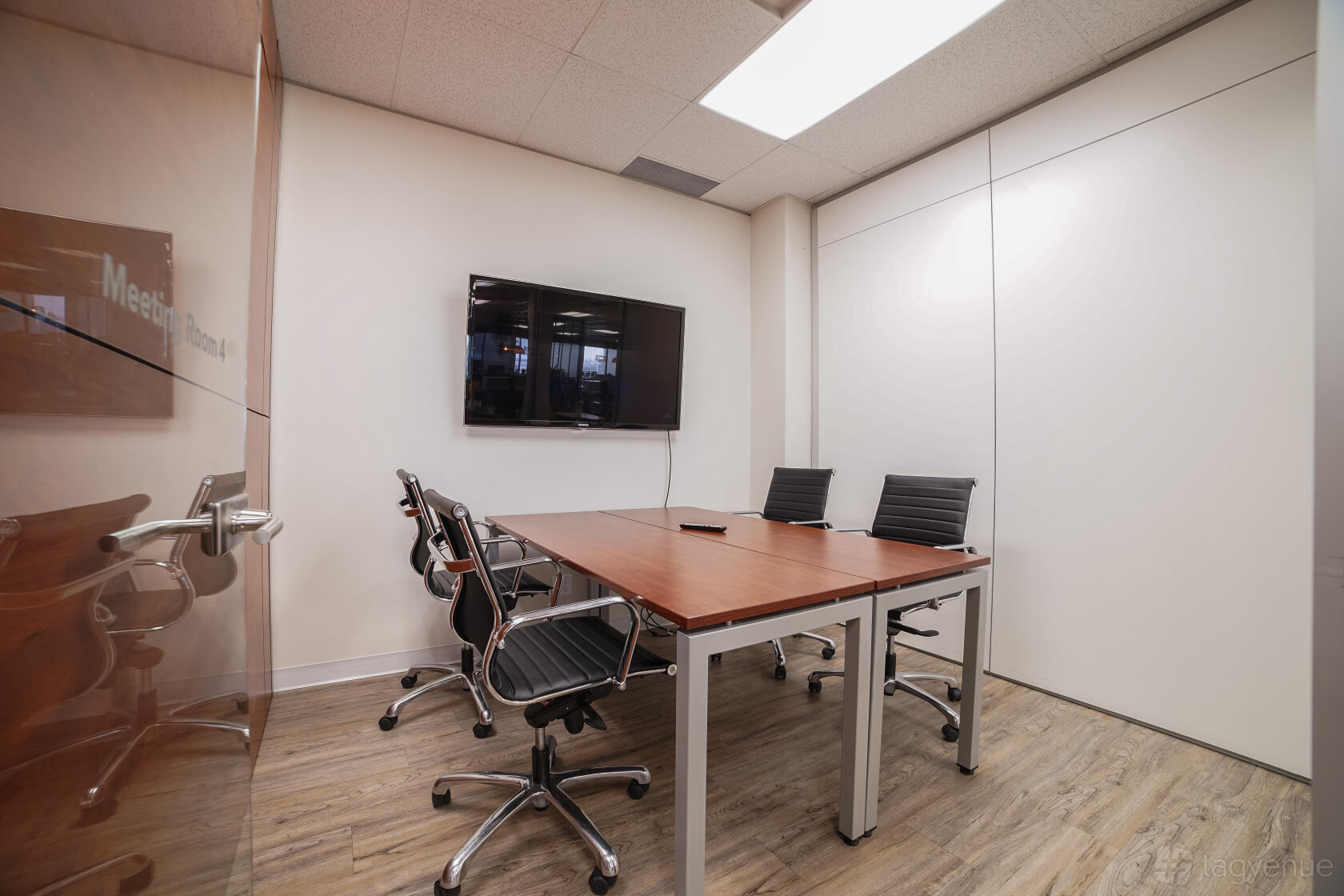 A coworking space with a wood table, black office chairs, and wall-mounted TV at Touchdown Coworking.