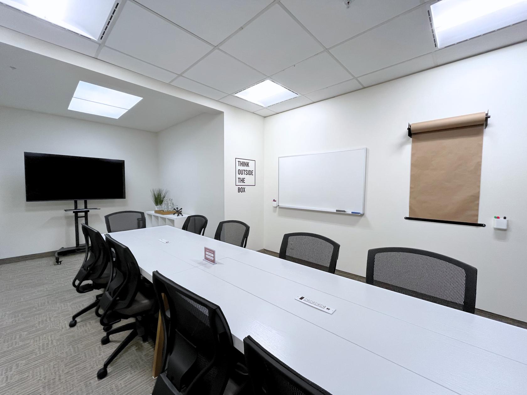 A meeting room with a long white conference table, modern chairs, a wall-mounted whiteboard, and a TV at The Professional Centre.