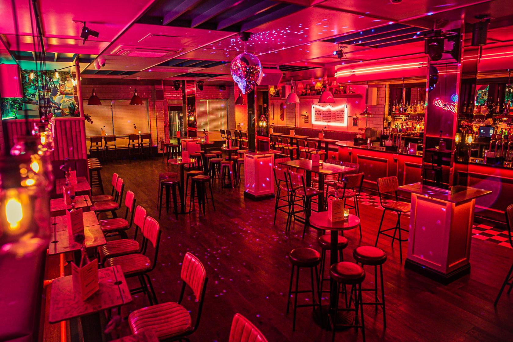 A function room in a cocktail bar with neon lighting, high tables, bar seating, and a disco ball at Simmons | Holborn.