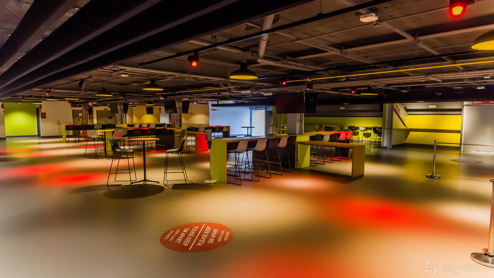 An event venue with high tables, bar stools, and painted flooring under exposed ceilings at Brentford Football Club.