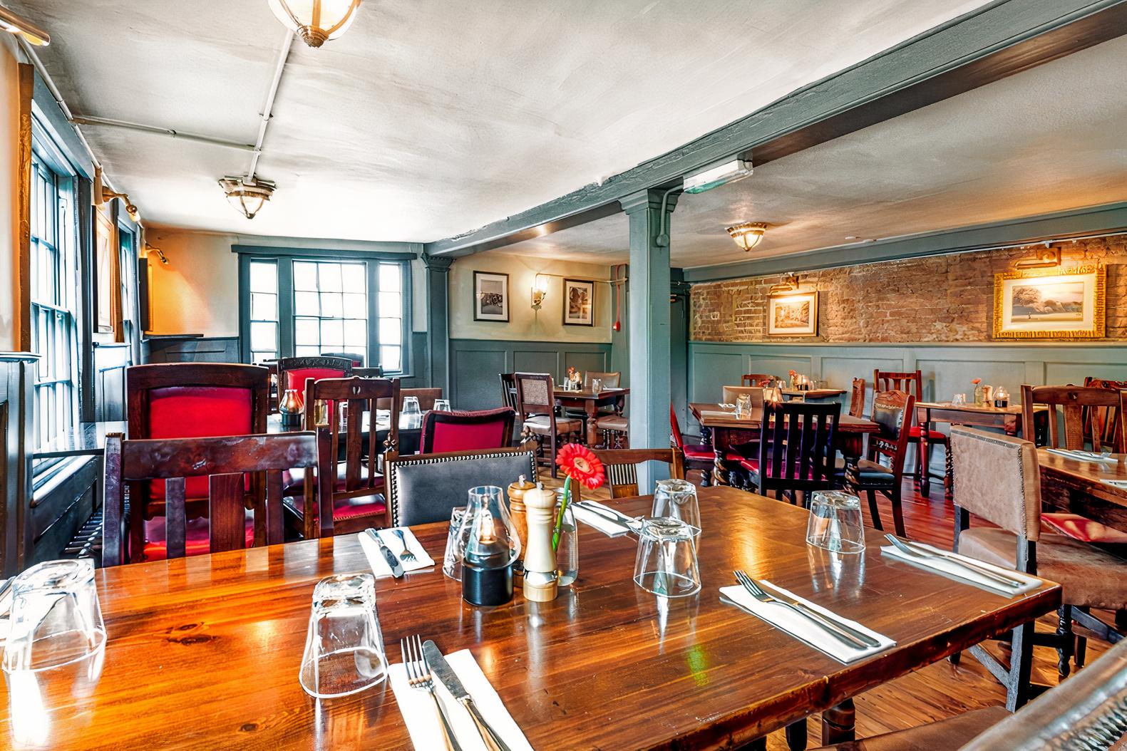 A dining room in a pub with wooden tables, red-upholstered chairs, exposed brickwork, and framed artwork at The Spaniards Inn.