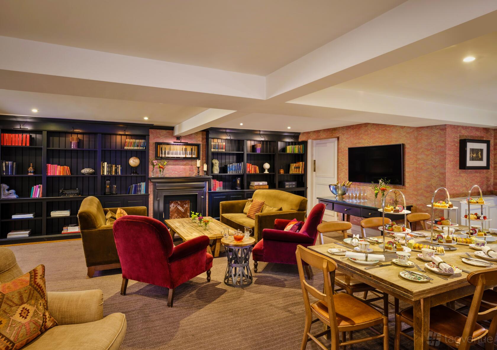 An event space with bookshelves, upholstered armchairs, a fireplace, and afternoon tea setup at King Street Townhouse.
