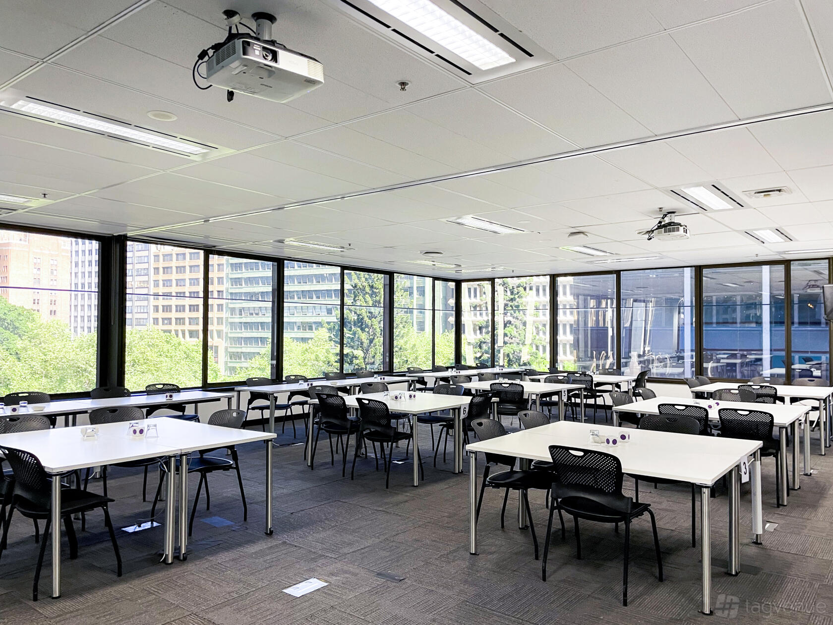 A conference centre with floor-to-ceiling windows, modular tables, black chairs, and city views at Cliftons Sydney Margaret St.