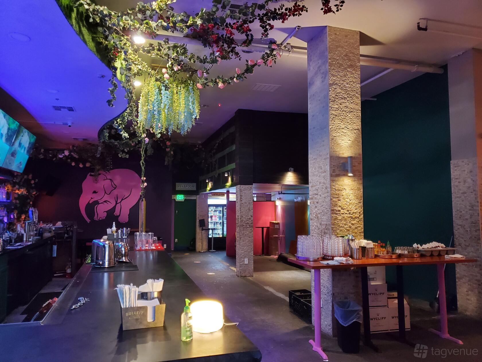 A restaurant with a floral ceiling installation, stone columns, and a bar counter at Pink Elephant.