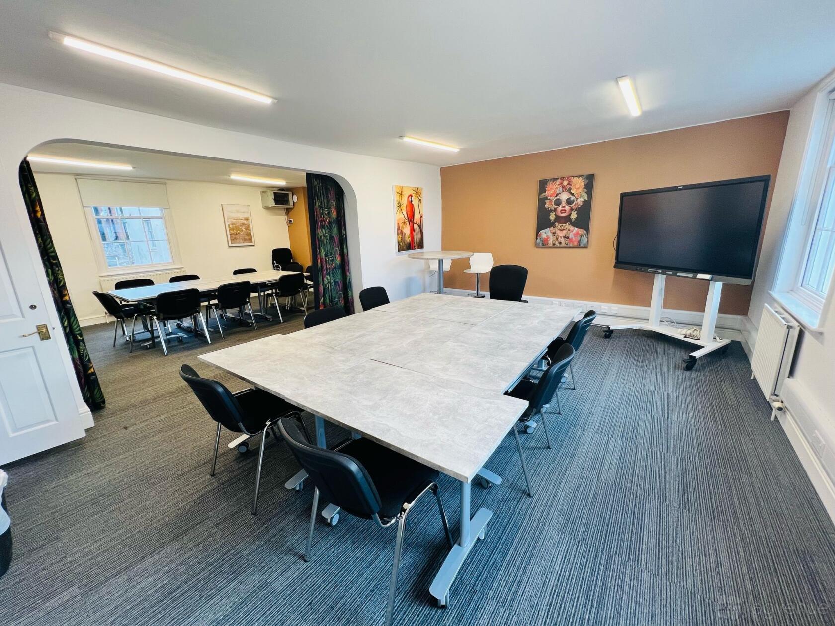An office space with conference tables, black chairs, wall art, and a large display screen at Burlington House.