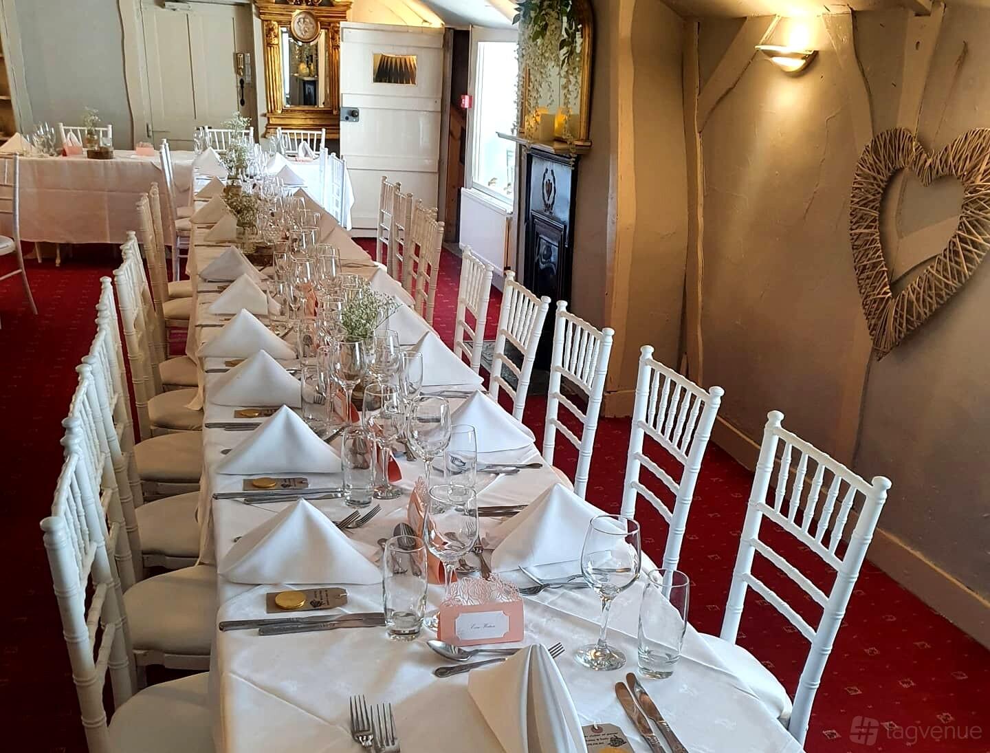 An event space with a long banquet table, white chairs, red carpet, and rustic wall decor at Royal Arms Hotel.