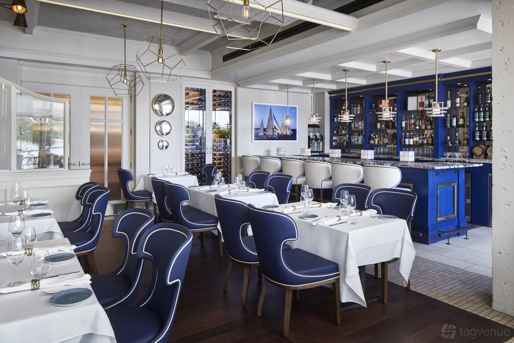 An event space in a restaurant with navy chairs, white tablecloths, and a blue mirrored bar at Fiola Mare.