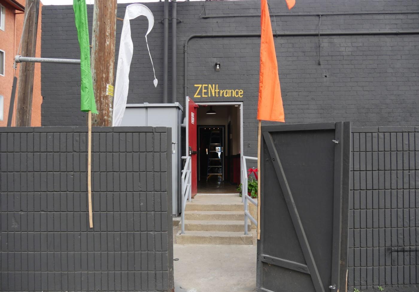 An entrance to a museum with black brick walls, flag banners, and an open gate at Surreal 3D Art Museum.