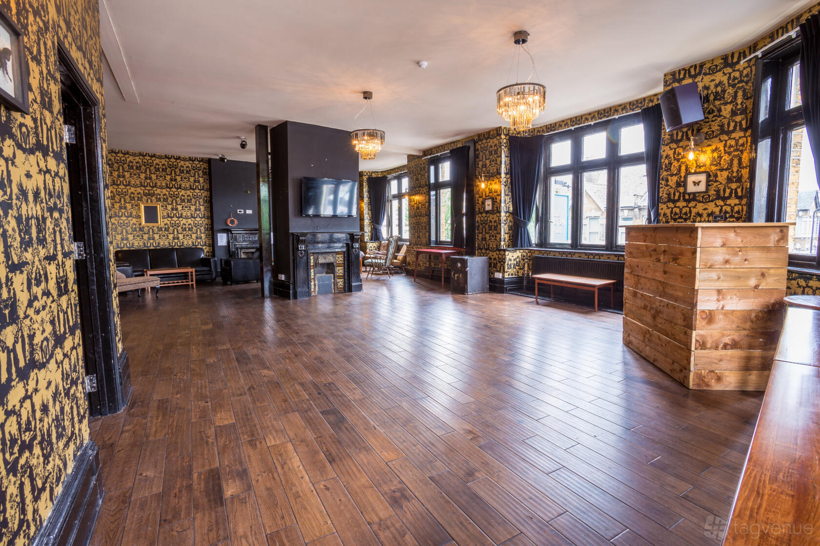 A function room in a pub with dark wood flooring, patterned wallpaper, chandeliers, and large windows at The Leyton Star.