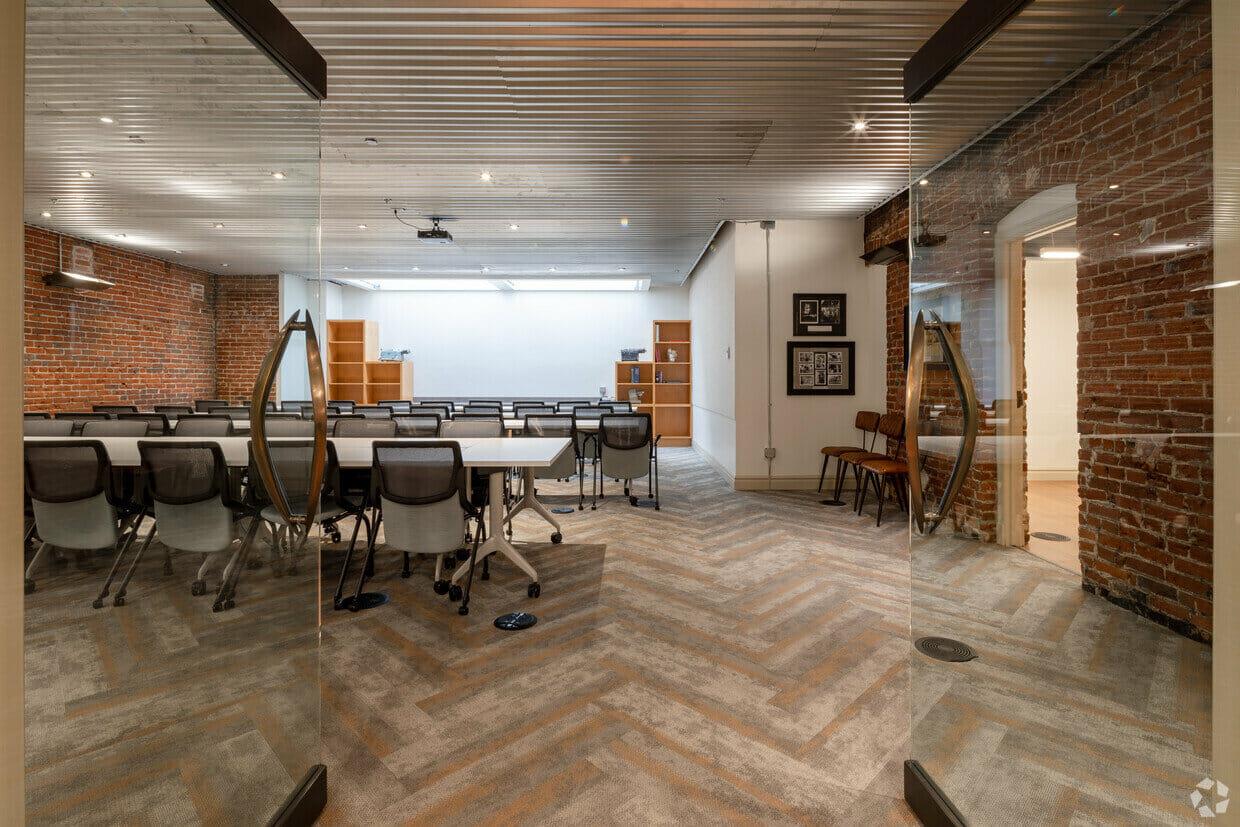 An event space with glass doors, exposed brick walls, herringbone flooring, and conference tables at Candy Factory CoWorking.