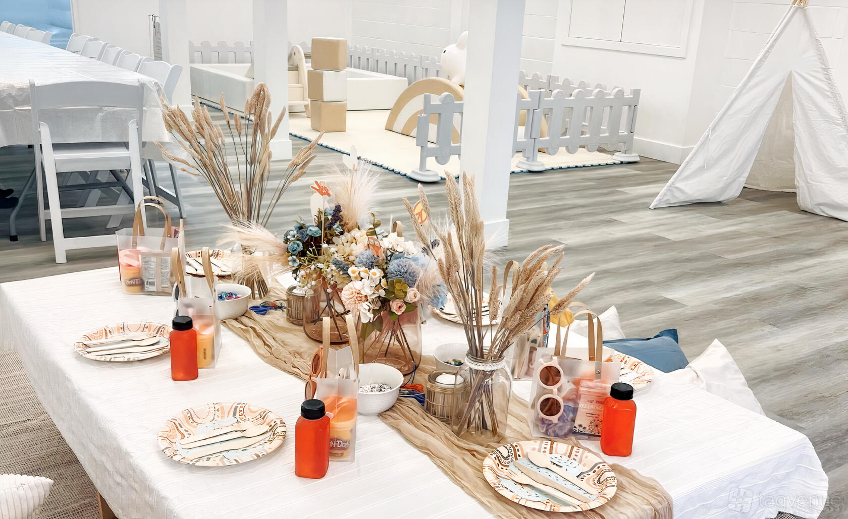 A function room with a long table set for guests, dried floral centerpieces, and kids’ play area at Contemporary and Modern Studio.