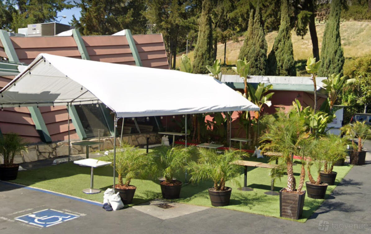 An outdoor patio with a white canopy, potted palms, and artificial turf at Mel's Drive-In West Hollywood.