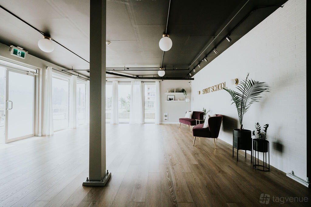 A training room with floor-to-ceiling windows, light wood floors, white walls, and lounge chairs at Squamish Retreats.