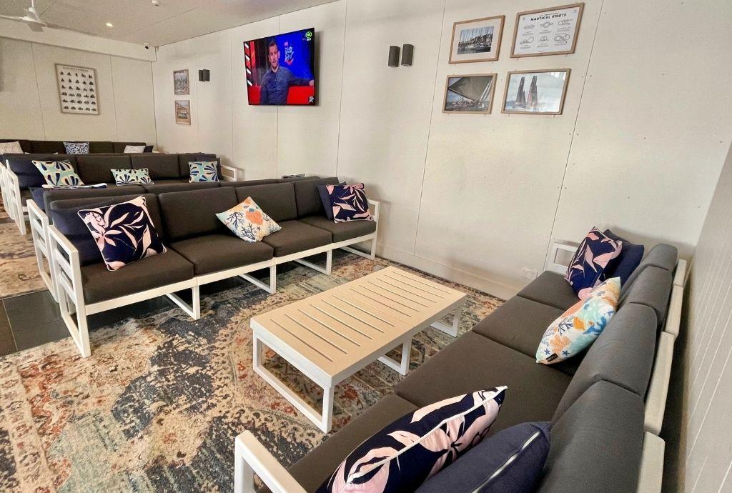 A bar lounge with cushioned sofas, patterned throw pillows, and a wall-mounted TV at Cockle Bay Yacht Club.