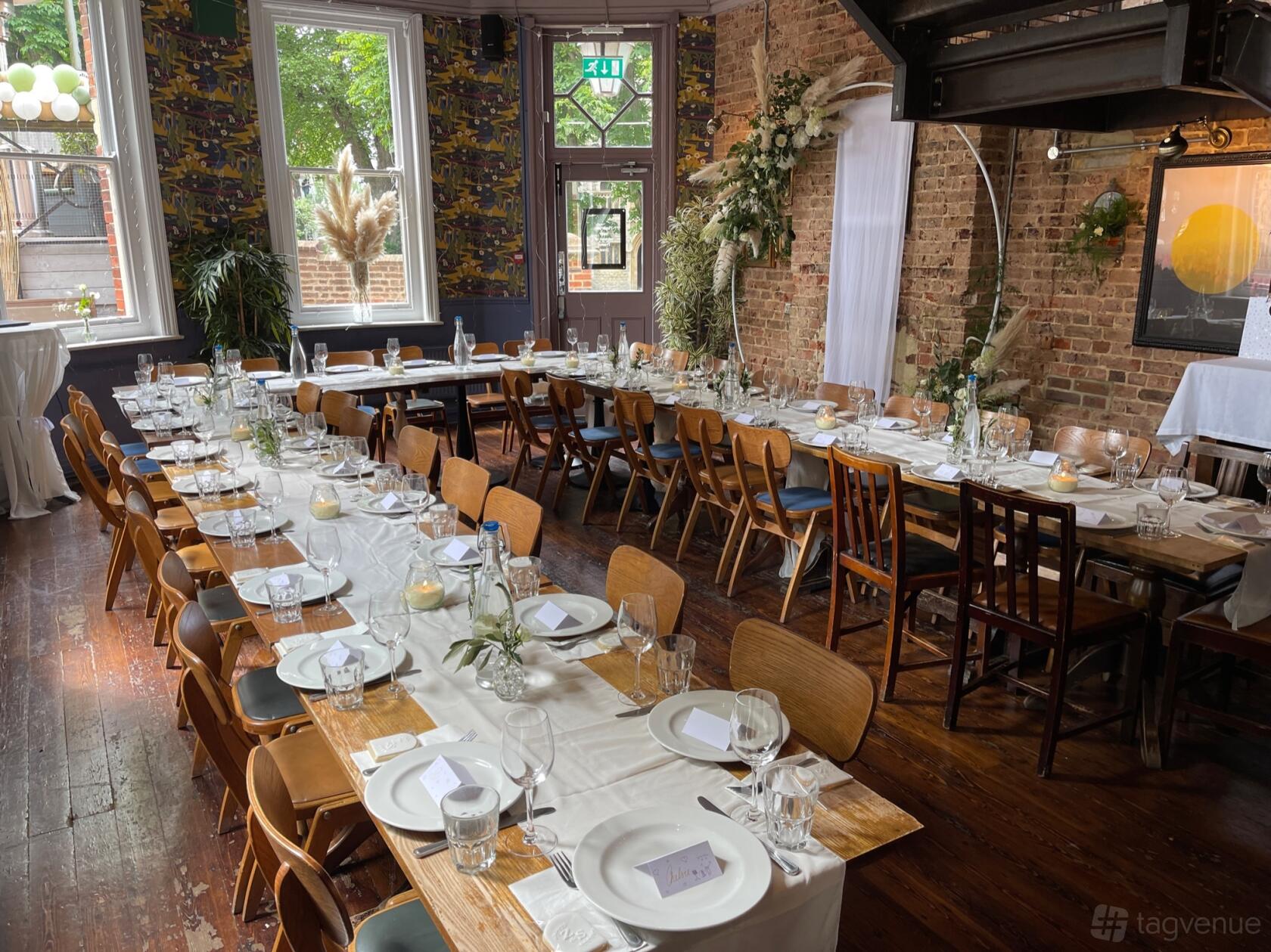 A pub with long banquet tables set with glassware, white linens, wooden chairs, and exposed brick walls at The Park View.