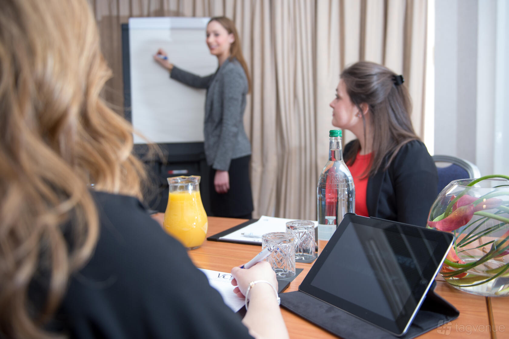 A meeting room with a flip chart, conference table set with water and juice, and an attendee using a tablet at Victory Services Club.