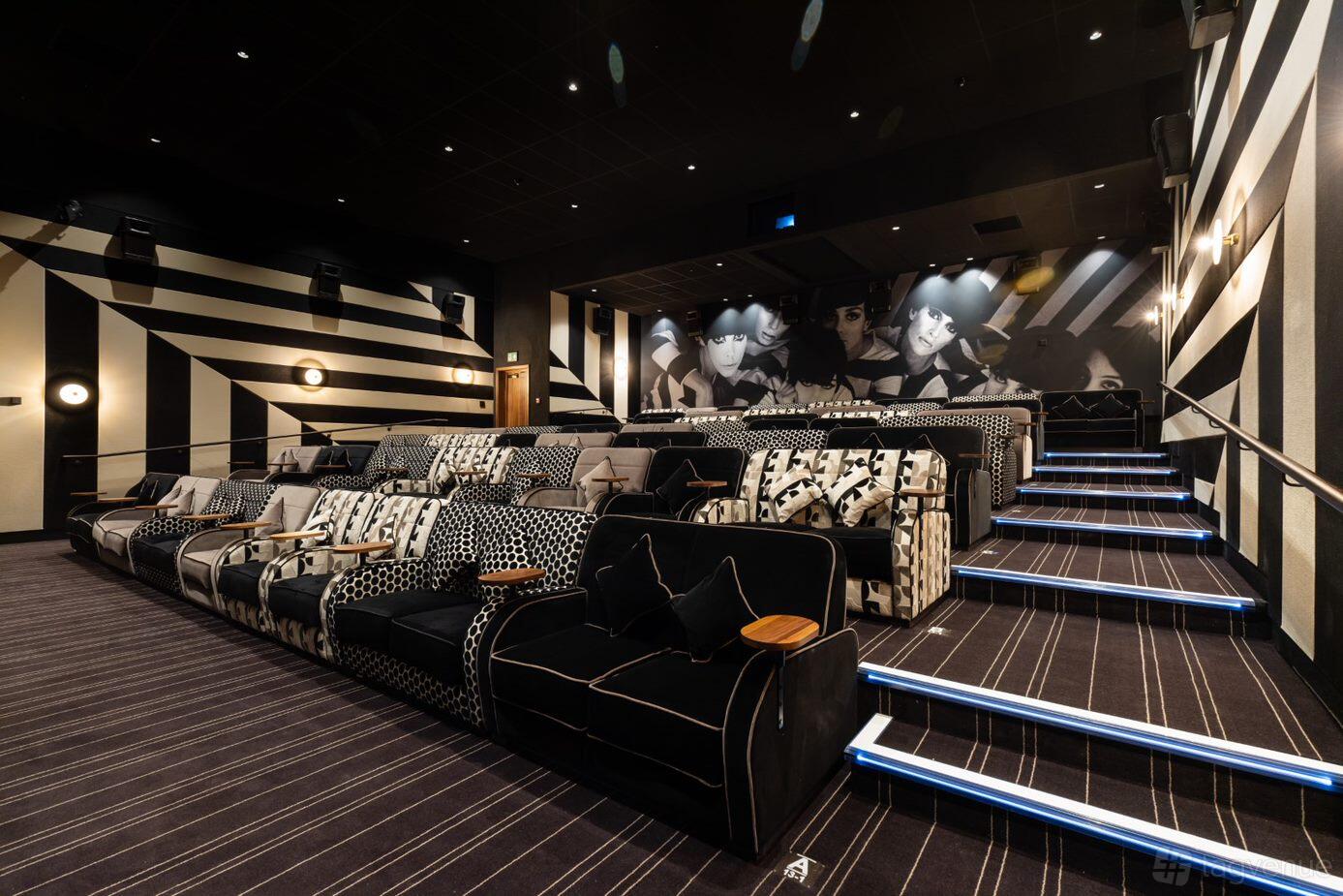 An auditorium with tiered sofa seating, patterned upholstery, aisle lighting, and monochrome wall art at Everyman Edinburgh.