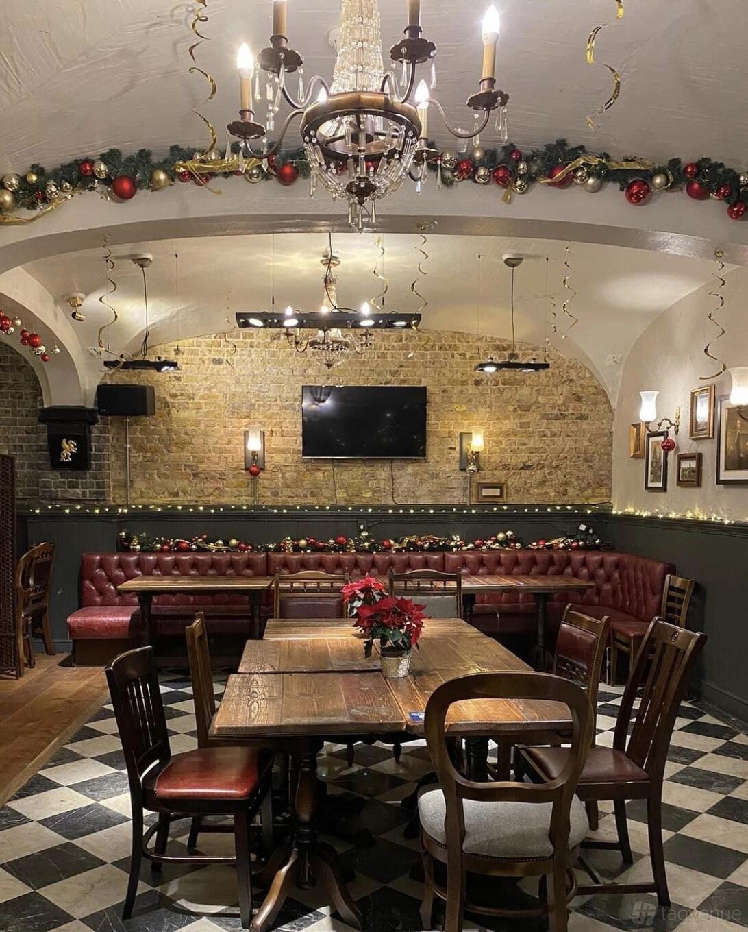 A pub dining room with exposed brick walls, red leather banquette seating, wooden tables, and festive decorations at The Williamson's Tavern.