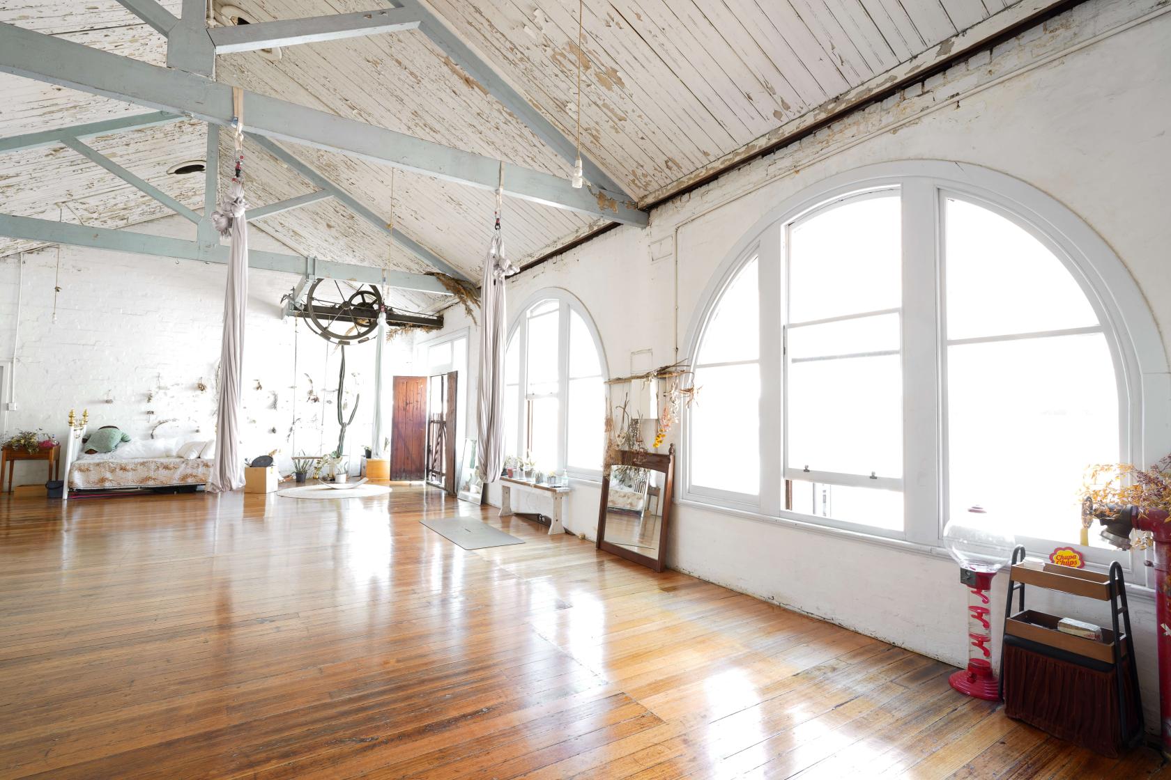 A loft with exposed timber beams, arched windows, and polished wood floors at CBD.