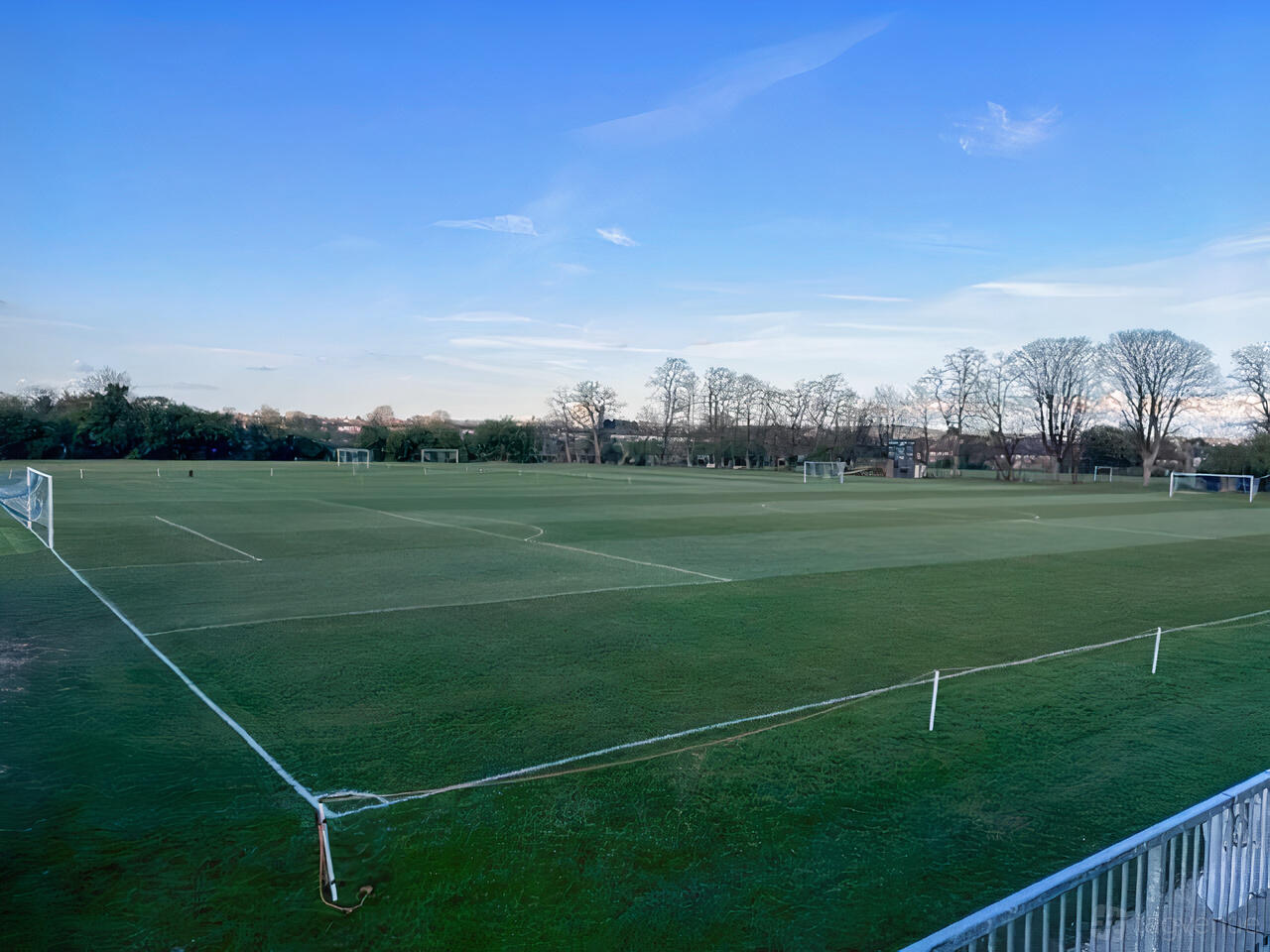 A sports hall with multiple outdoor football pitches, goalposts, and surrounding trees at Club Rooms.