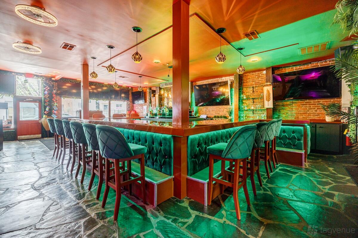 A restaurant with a U-shaped bar, tufted green barstools, exposed brick walls, and colorful accent lighting at Miss Conduck.