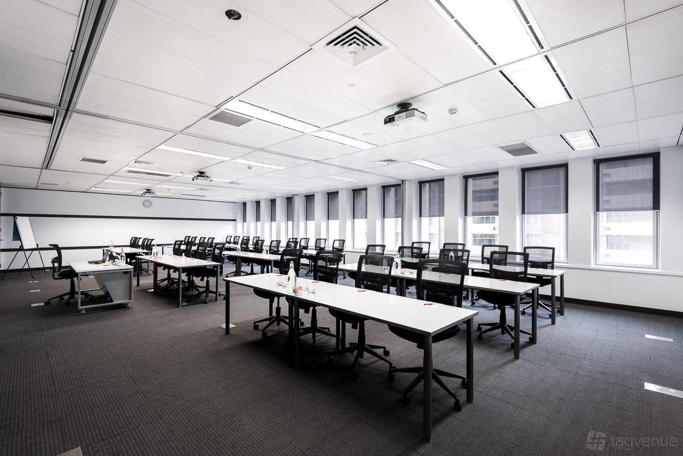 A meeting room with rows of black chairs, long white tables, and ceiling-mounted projectors at Cliftons Perth.