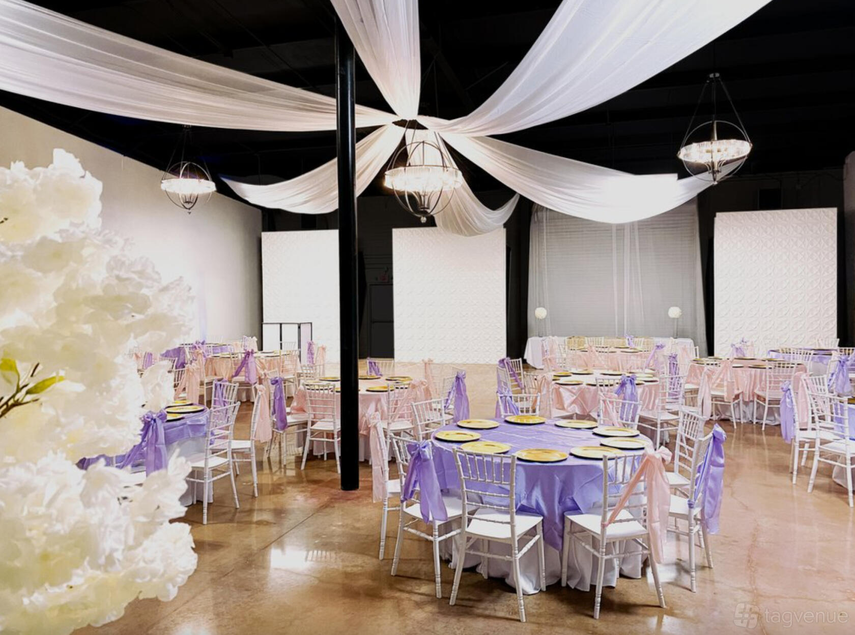 An event venue with draped white fabric ceiling, chandeliers, and round tables with lilac linens at The Modern Event Space.