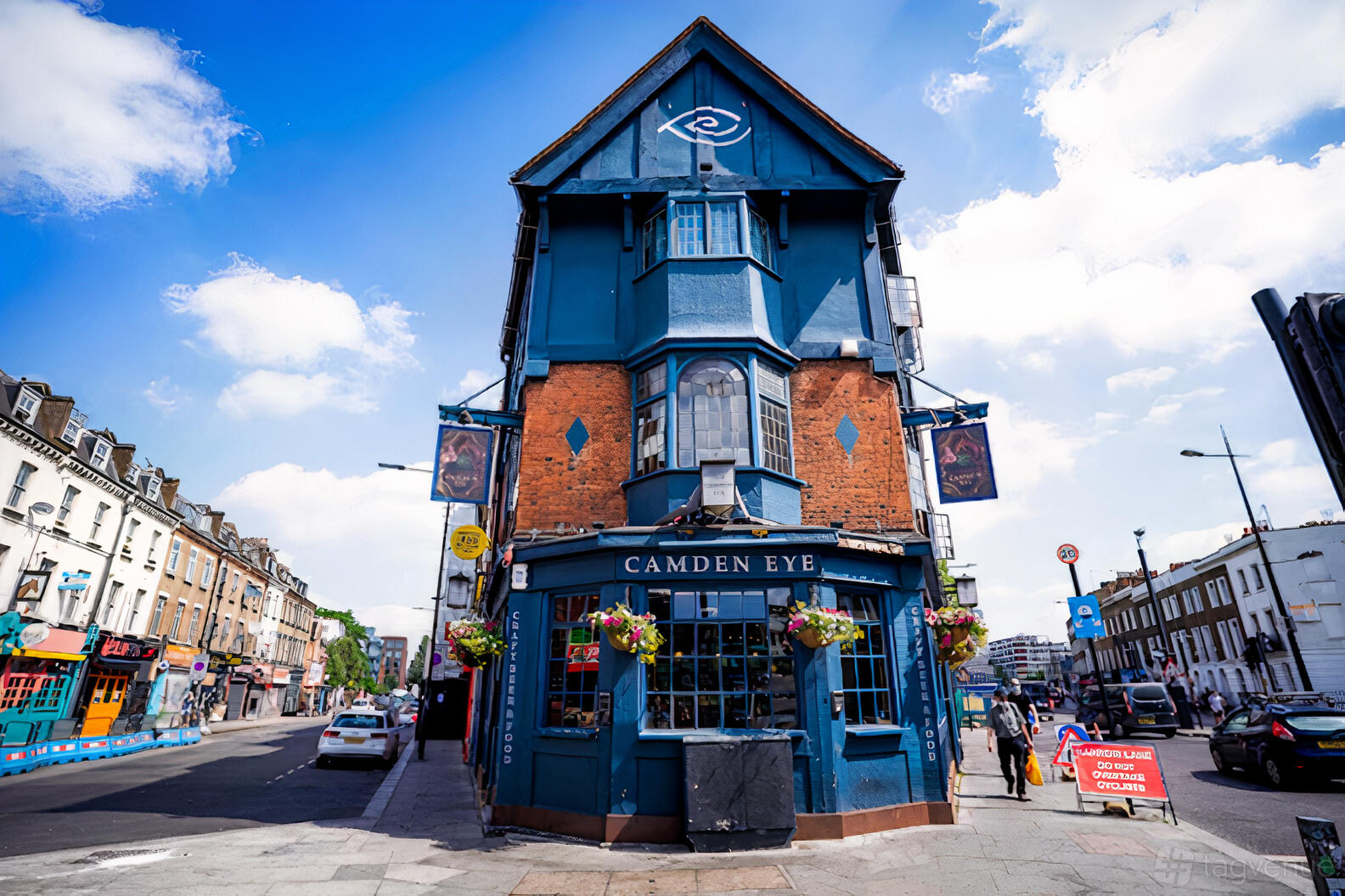 A pub with a distinctive blue exterior, hanging flower baskets, and large street-facing windows at The Camden Eye.